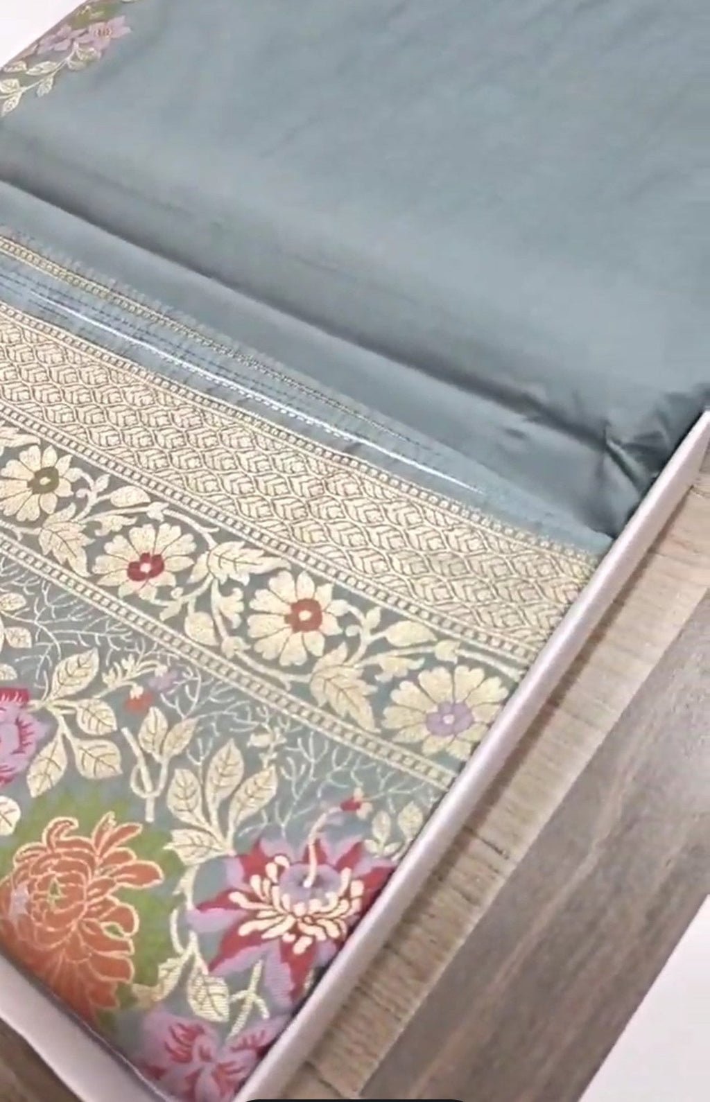 A serene powder blue Banarasi semi Katan silk saree with a plain body, a multi-colored Tilfi Meenakari floral border, and a matching heavy brocade blouse.