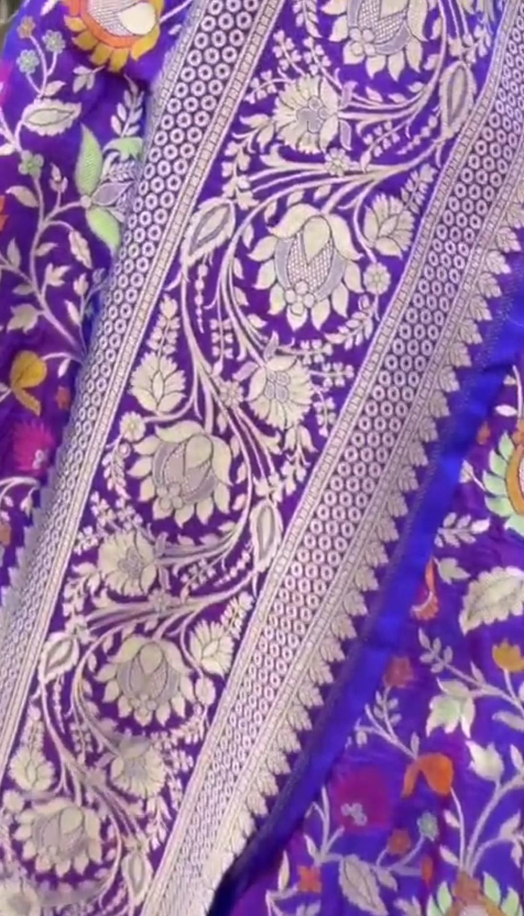 A deep purple Banarasi Katan silk saree featuring vibrant three-colored Tilfi Meenakari floral buttas and an ornate gold zari border.