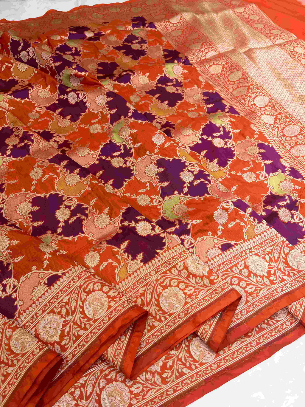A vibrant chilly red Banarasi Katan silk saree featuring rare Rangkaat diagonal color blocking and multi-hued Meenakari floral weaving.