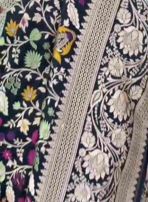 A royal black Banarasi Katan silk saree featuring colorful Tilfi Meenakari floral buttas and an intricate gold zari border.