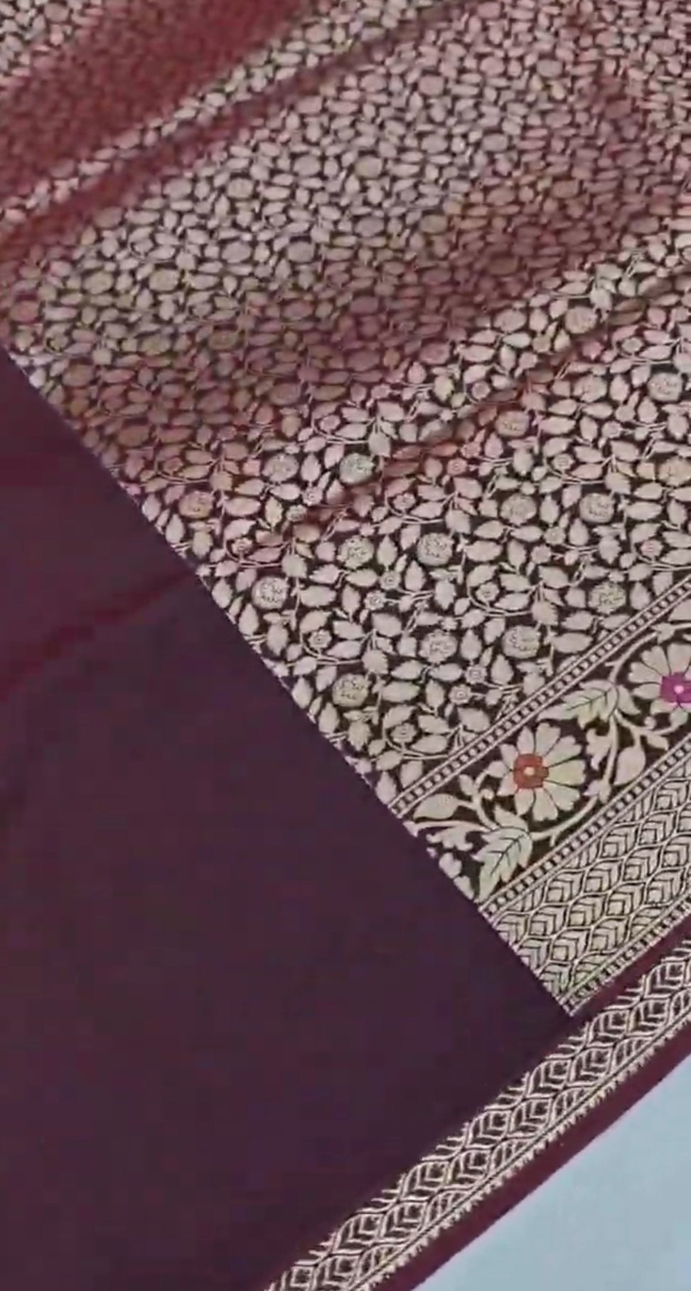 A deep wine-colored Banarasi semi Katan silk saree with a minimalist plain body, intricate Tilfi Meenakari floral borders, and a heavy gold zari blouse.