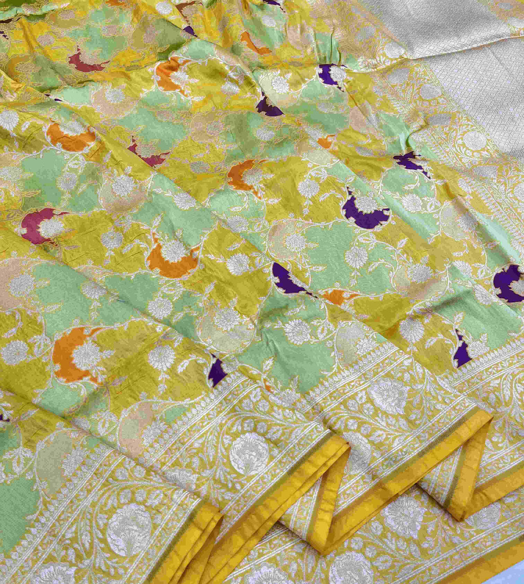 A luminous golden yellow Banarasi Katan silk saree with hand-woven Rangkaat diagonal patterns and vibrant multi-colored Meenakari floral vines.