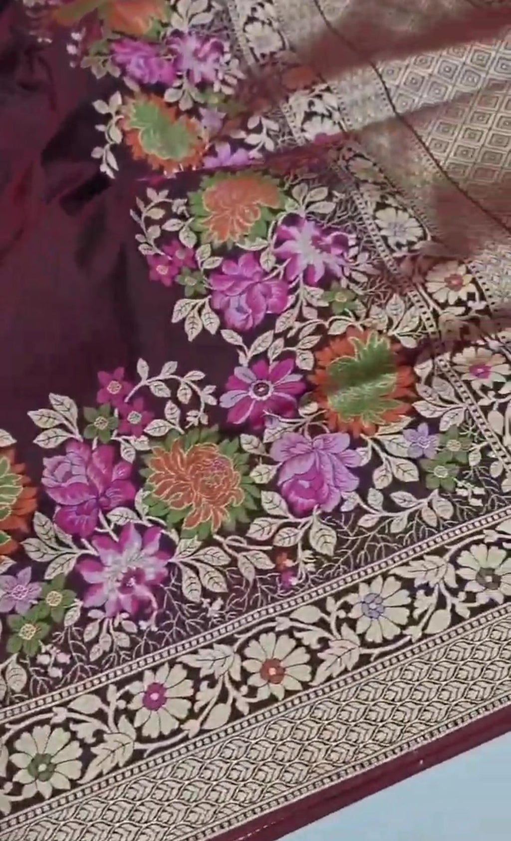 A deep wine-colored Banarasi semi Katan silk saree with a minimalist plain body, intricate Tilfi Meenakari floral borders, and a heavy gold zari blouse.