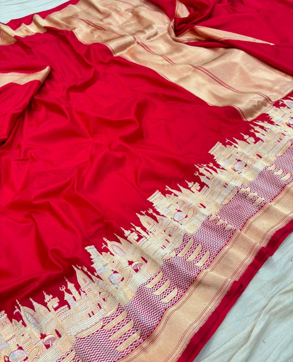 A vibrant red Banarasi Katan silk saree with a handloom-woven Kashi Ghat temple motif border in gold and silver zari with Meenakari accents.