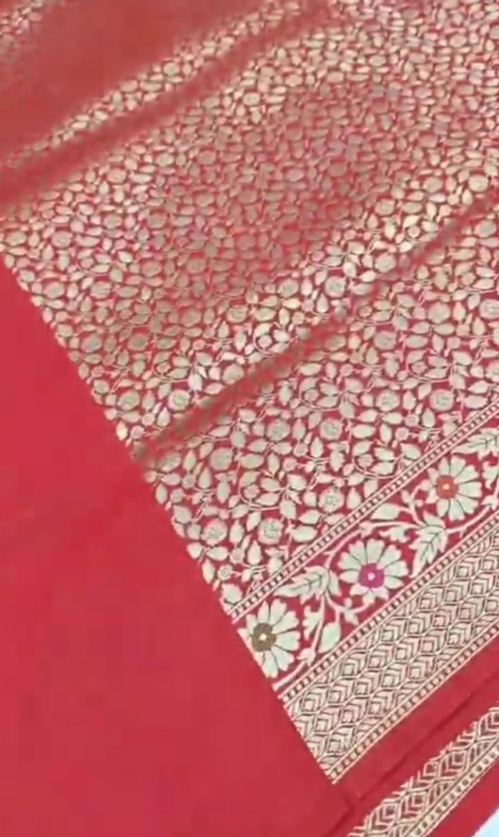 A bright bridal red Banarasi semi Katan silk saree with a minimalist plain body, intricate Tilfi Meenakari floral borders, and a heavy gold zari brocade blouse.