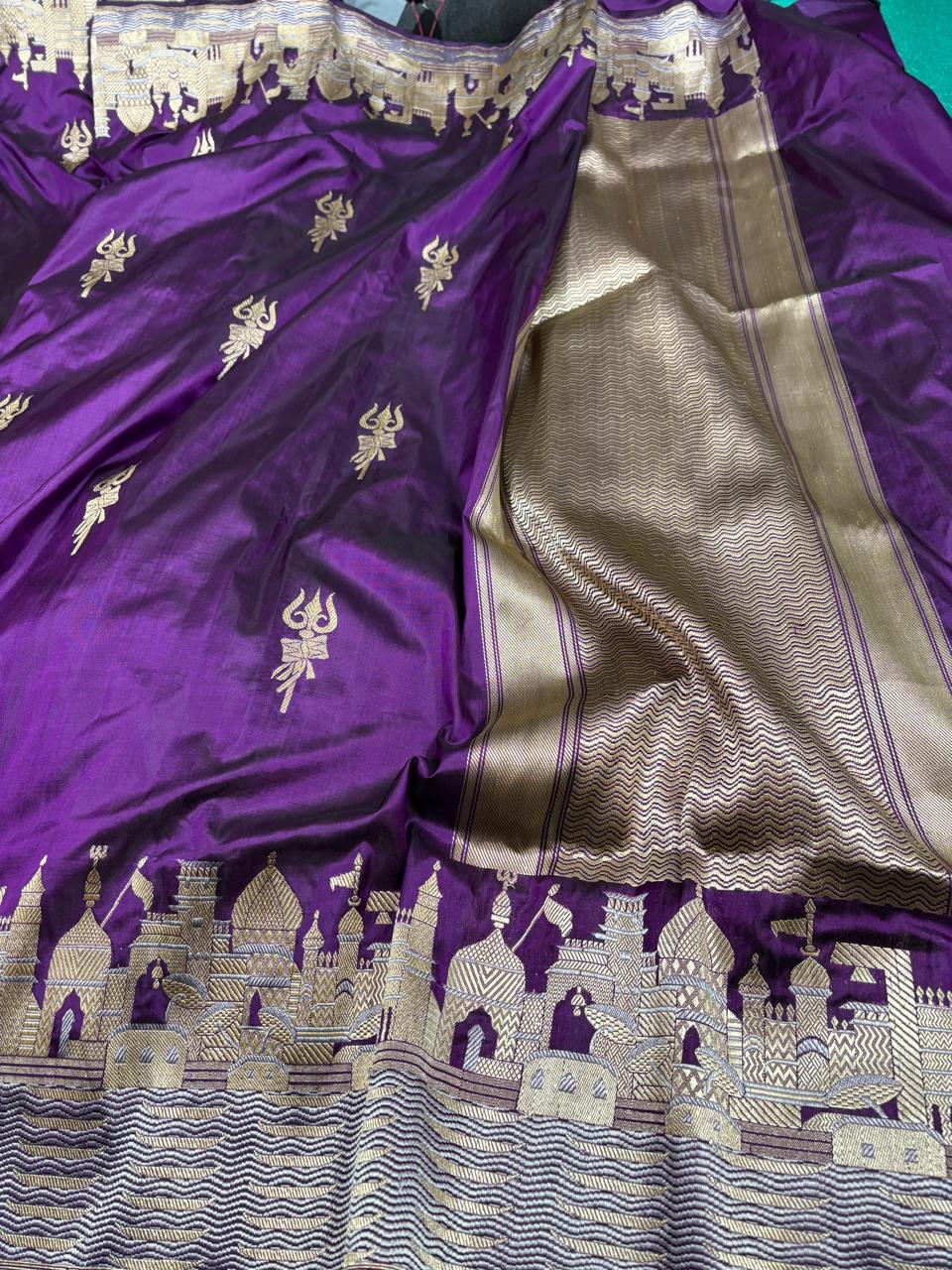 Royal purple Katan silk saree featuring gold zari Damru and Trishul motifs on the body and an intricate Kashi Ghat temple border.
