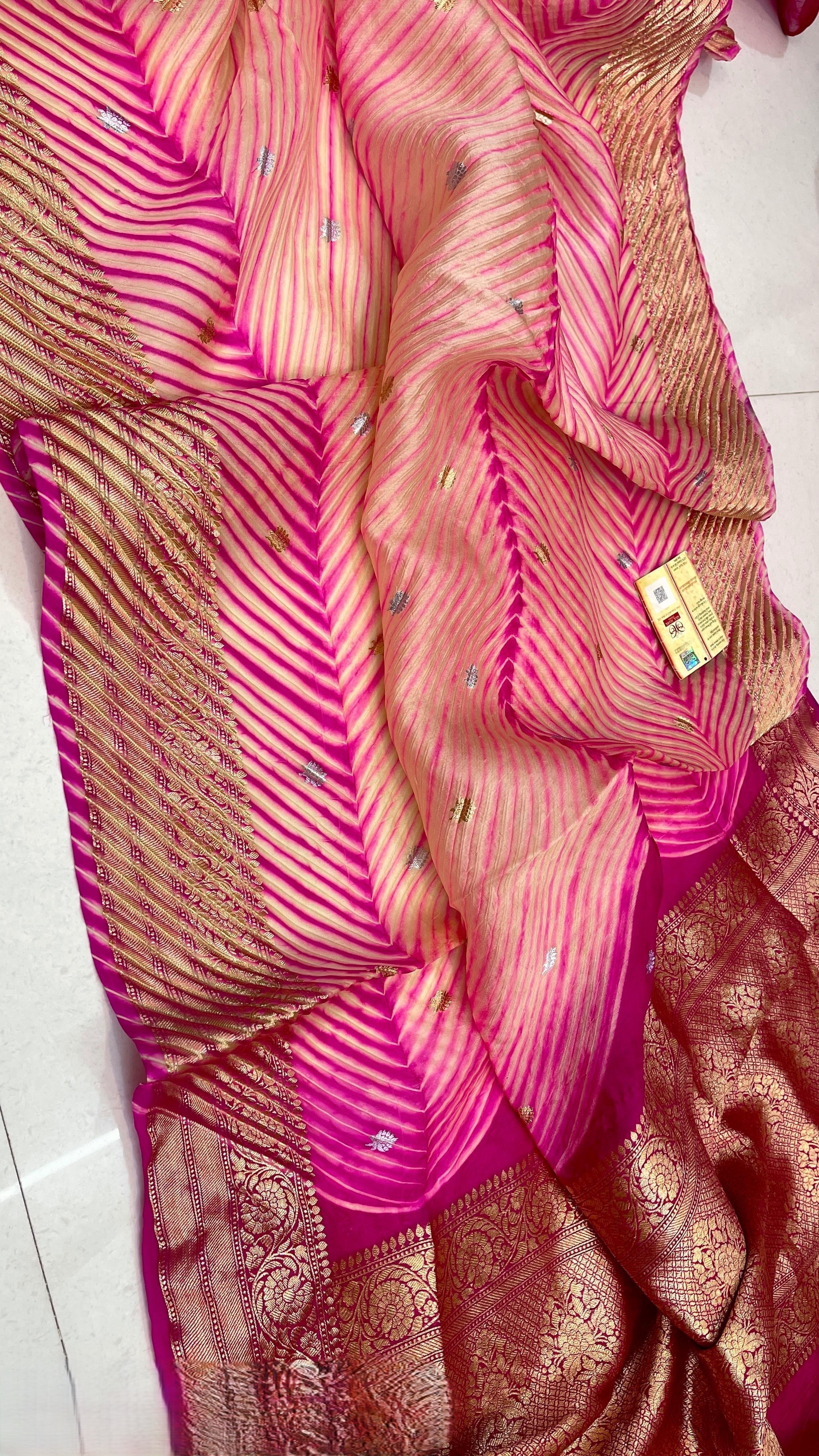A model in a heritage courtyard wearing a vibrant Pink and Magenta Kora Tissue silk saree with hand-dyed diagonal Arasi Shibori patterns and a gold zari border.