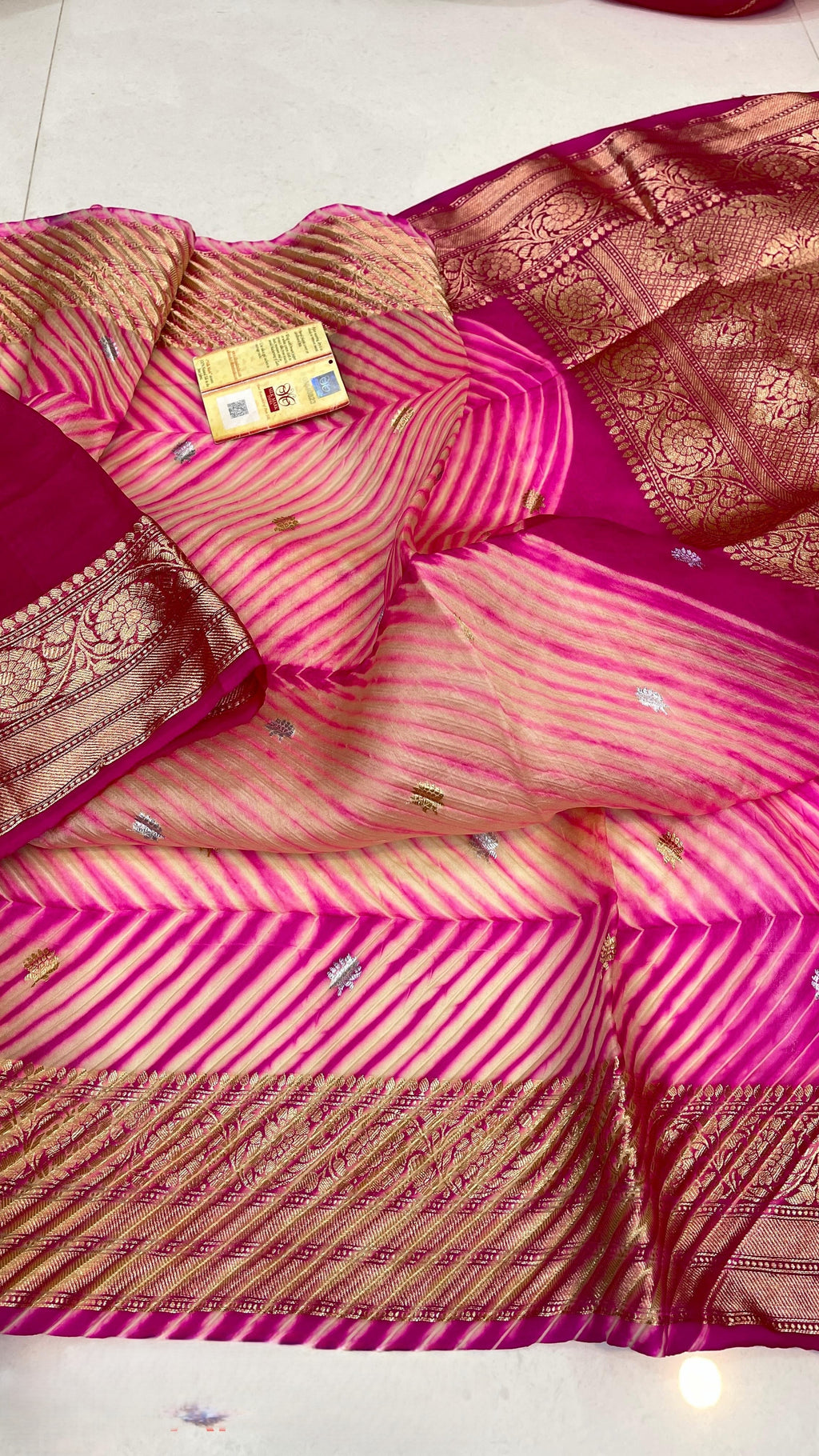 A model in a heritage courtyard wearing a vibrant Pink and Magenta Kora Tissue silk saree with hand-dyed diagonal Arasi Shibori patterns and a gold zari border.