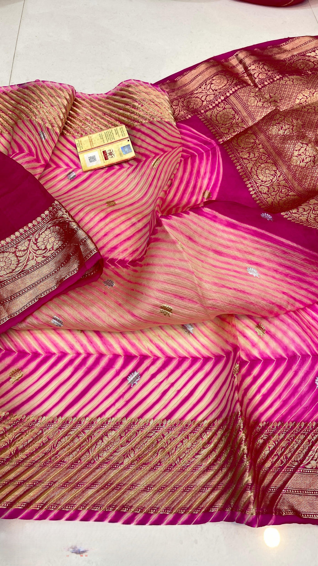 A model in a heritage courtyard wearing a vibrant Pink and Magenta Kora Tissue silk saree with hand-dyed diagonal Arasi Shibori patterns and a gold zari border.