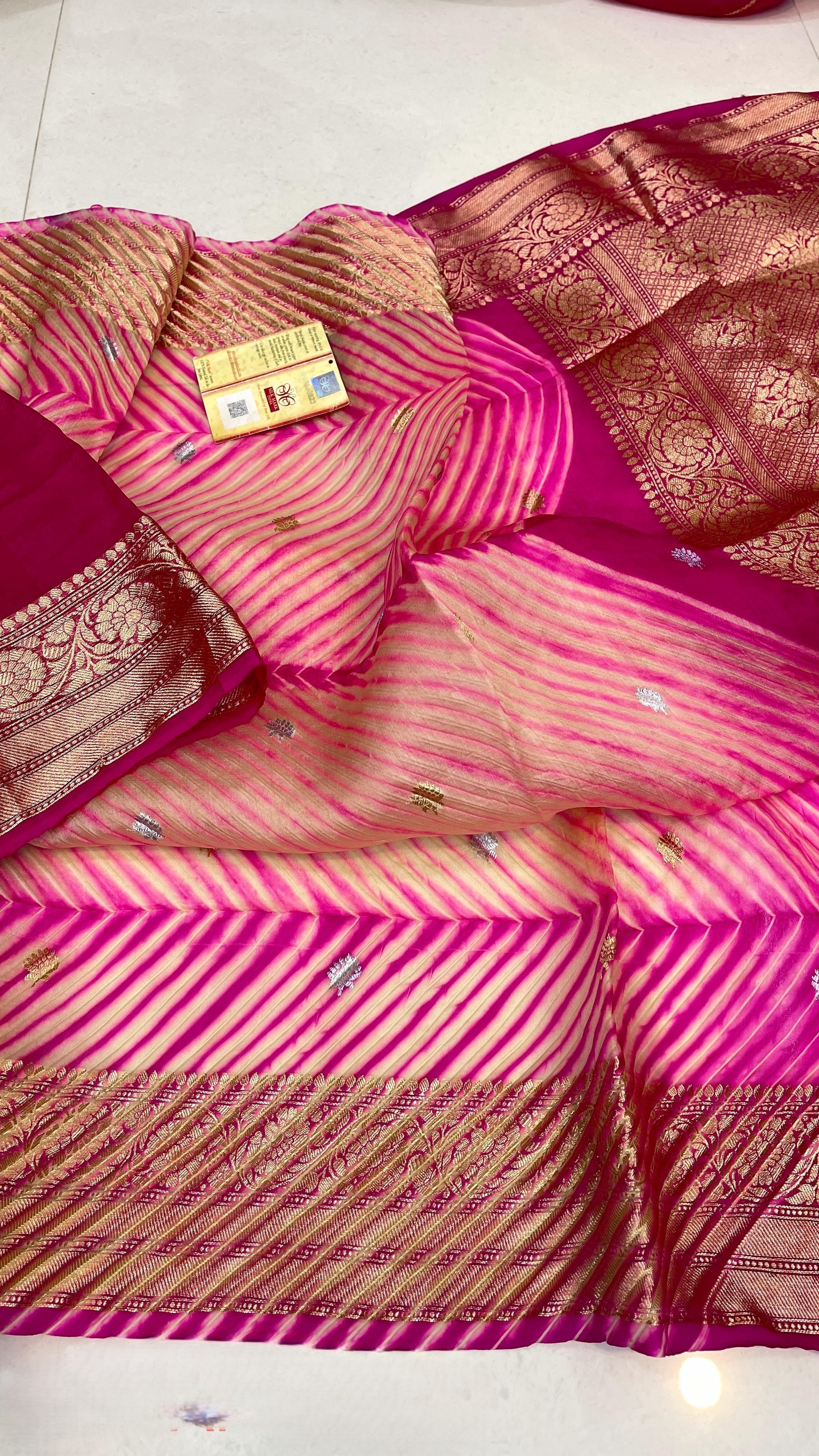 A model in a heritage courtyard wearing a vibrant Pink and Magenta Kora Tissue silk saree with hand-dyed diagonal Arasi Shibori patterns and a gold zari border.
