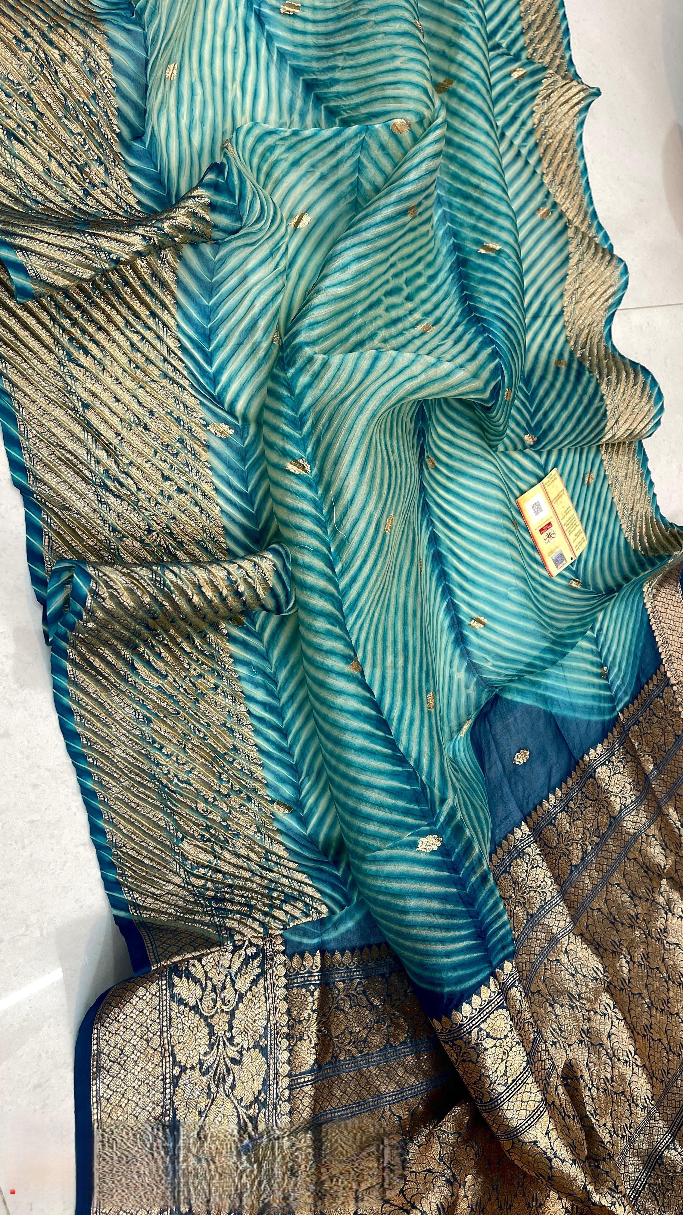 Two models in a Banarasi courtyard. One standing and the other sitting on a step. They are wearing a handloom Kora Tissue silk saree with turquoise and green hand-dyed Arasi Shibori patterns and a gold and silver zari border and pallu.
