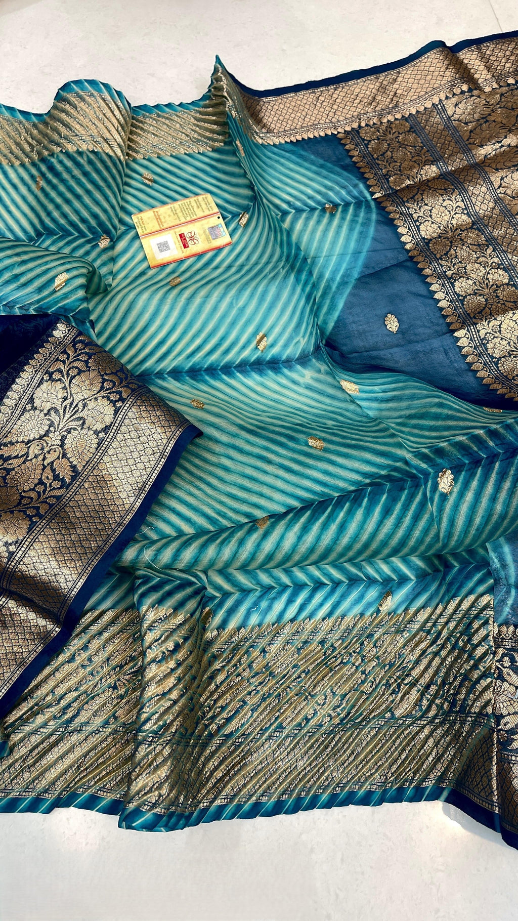 Two models in a Banarasi courtyard. One standing and the other sitting on a step. They are wearing a handloom Kora Tissue silk saree with turquoise and green hand-dyed Arasi Shibori patterns and a gold and silver zari border and pallu.