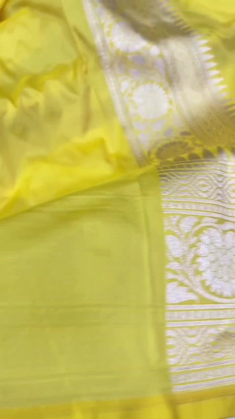 A vibrant turmeric yellow Banarasi handloom pure Katan silk saree with multicolored Meenakari floral bootis and a rich silver zari border, ideal for Haldi functions.