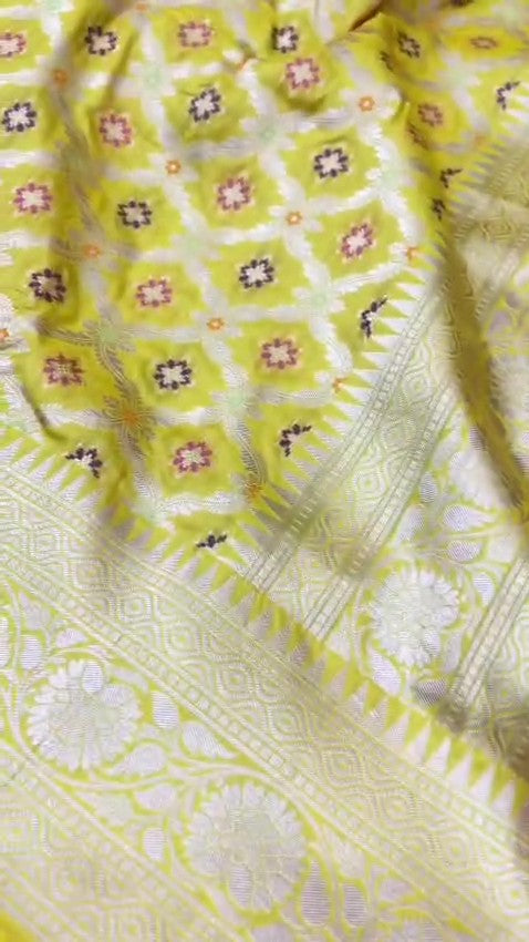 A vibrant turmeric yellow Banarasi handloom pure Katan silk saree with multicolored Meenakari floral bootis and a rich silver zari border, ideal for Haldi functions.