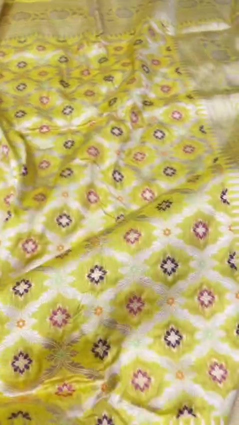 A vibrant turmeric yellow Banarasi handloom pure Katan silk saree with multicolored Meenakari floral bootis and a rich silver zari border, ideal for Haldi functions.