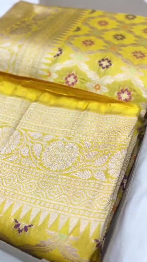 A vibrant turmeric yellow Banarasi handloom pure Katan silk saree with multicolored Meenakari floral bootis and a rich silver zari border, ideal for Haldi functions.