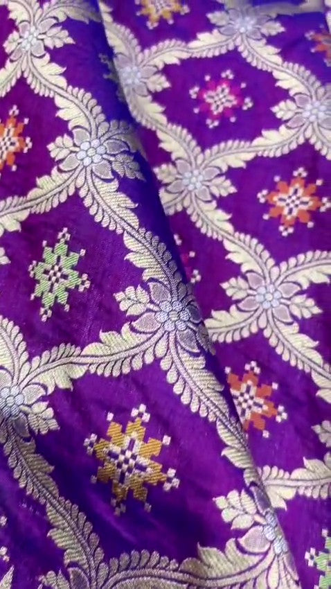 A deep royal purple Banarasi handloom pure Katan silk saree featuring vibrant multicolored Meenakari floral motifs and an elaborate silver zari border and pallu.
