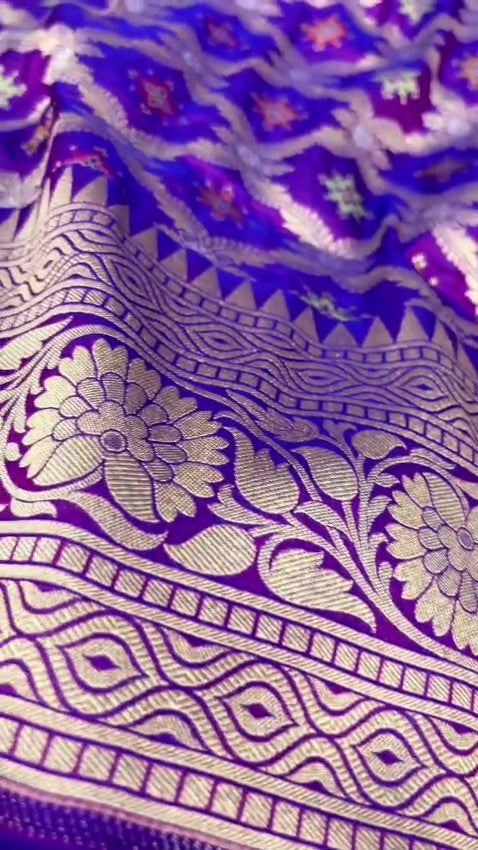 A deep royal purple Banarasi handloom pure Katan silk saree featuring vibrant multicolored Meenakari floral motifs and an elaborate silver zari border and pallu.
