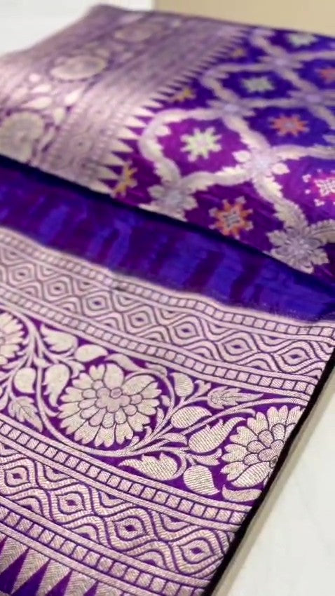 A deep royal purple Banarasi handloom pure Katan silk saree featuring vibrant multicolored Meenakari floral motifs and an elaborate silver zari border and pallu.
