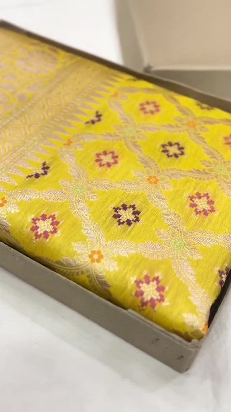 A vibrant turmeric yellow Banarasi handloom pure Katan silk saree with multicolored Meenakari floral bootis and a rich silver zari border, ideal for Haldi functions.