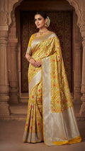 A model wearing a radiant yellow Banarasi handloom pure katan silk saree featuring intricate gold zari and meenakari weaving, posed against a traditional heritage archway background.