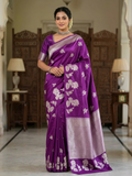 A model presenting a luxurious purple Banarasi Mashru silk saree featuring extensive silver zari floral motifs, a geometric zig-zag border, and a coordinating silver-bordered blouse in a regal heritage setting.