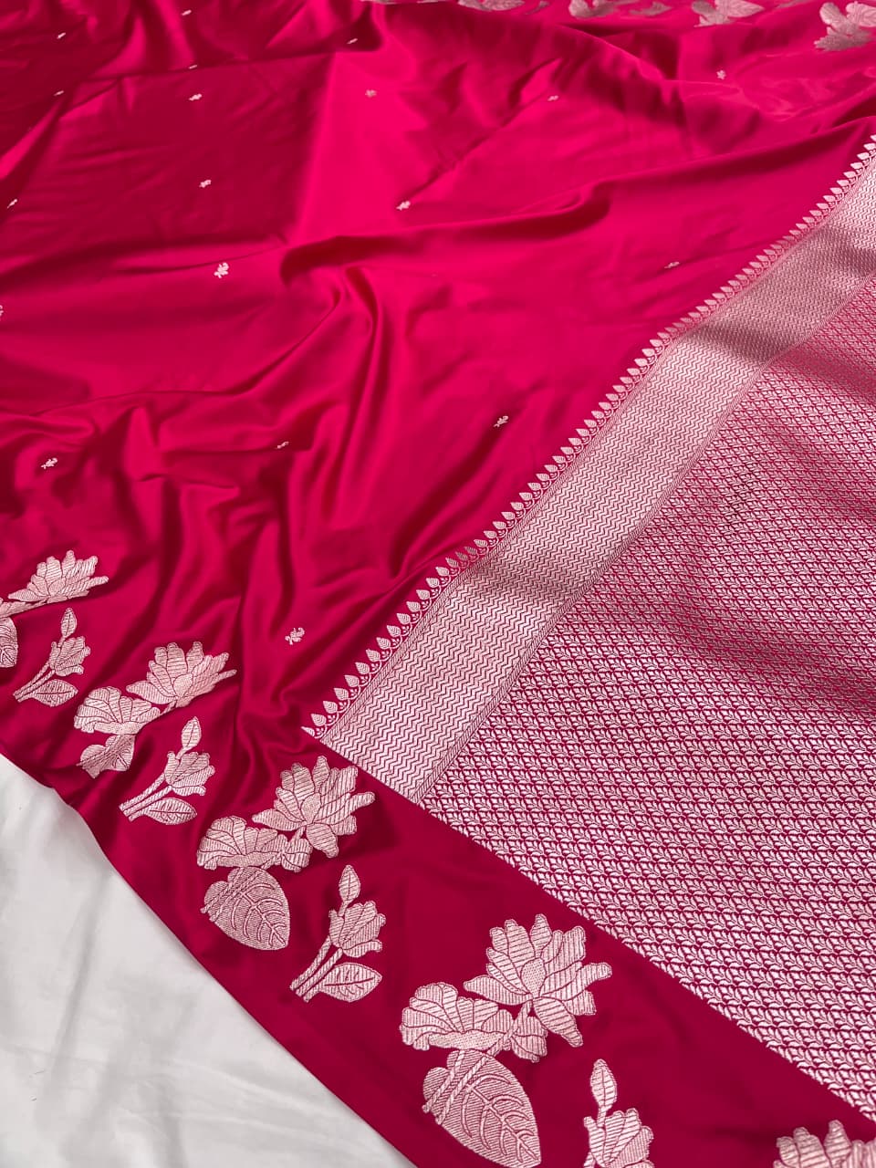 A model gracefully presenting a luxurious hot pink Banarasi Mashru silk saree adorned with intricate silver zari floral motifs and a detailed geometric border.