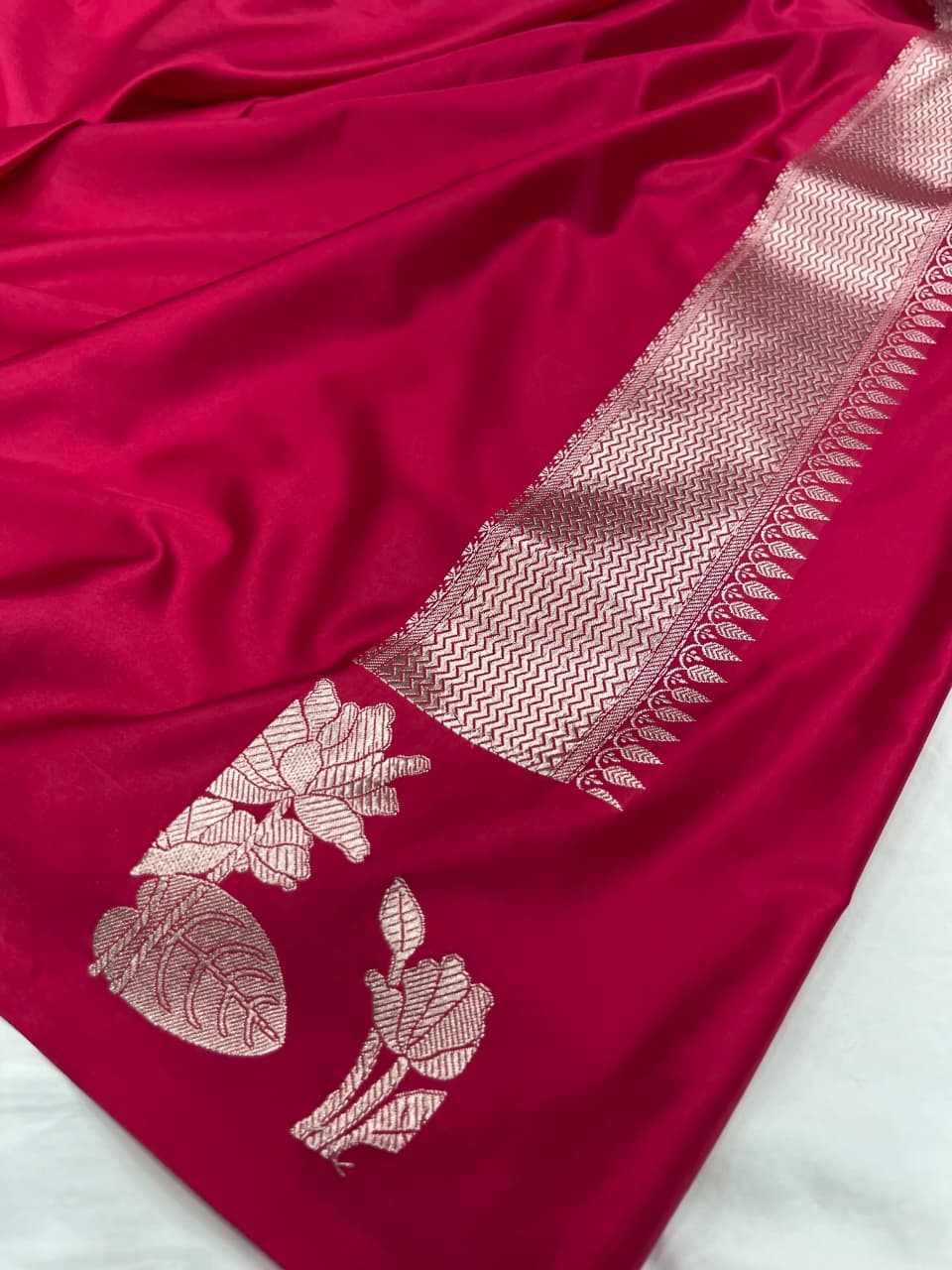 A model gracefully presenting a luxurious hot pink Banarasi Mashru silk saree adorned with intricate silver zari floral motifs and a detailed geometric border.