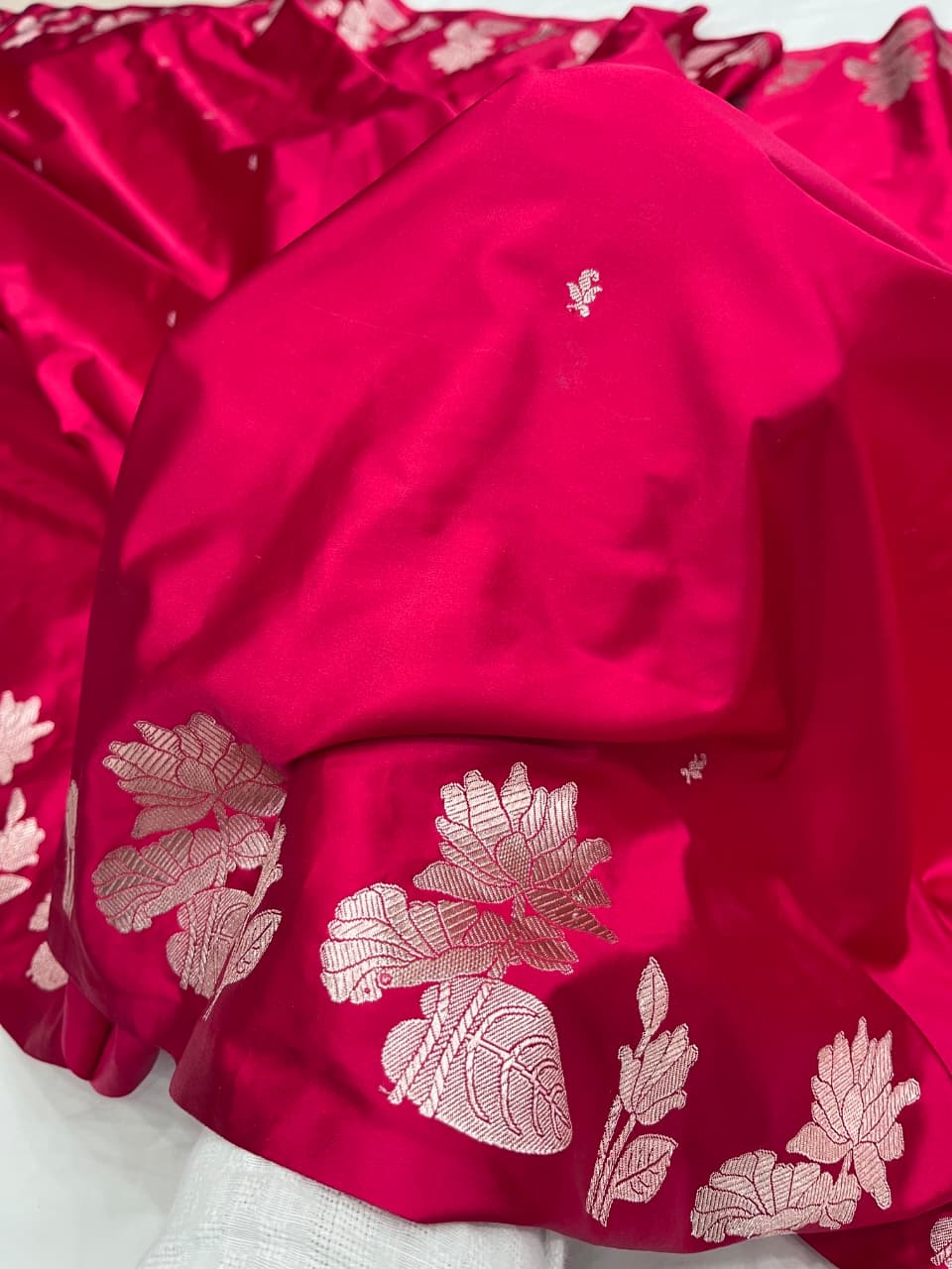 A model gracefully presenting a luxurious hot pink Banarasi Mashru silk saree adorned with intricate silver zari floral motifs and a detailed geometric border.