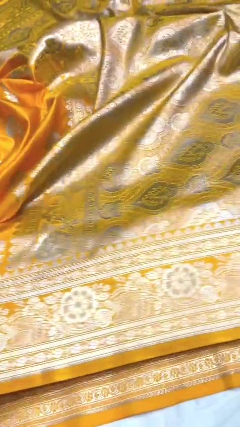 Radiant golden yellow Banarasi Mashru soft silk saree featuring intricate silver and gold zari work, a heavy floral border, and classic woven buttis.