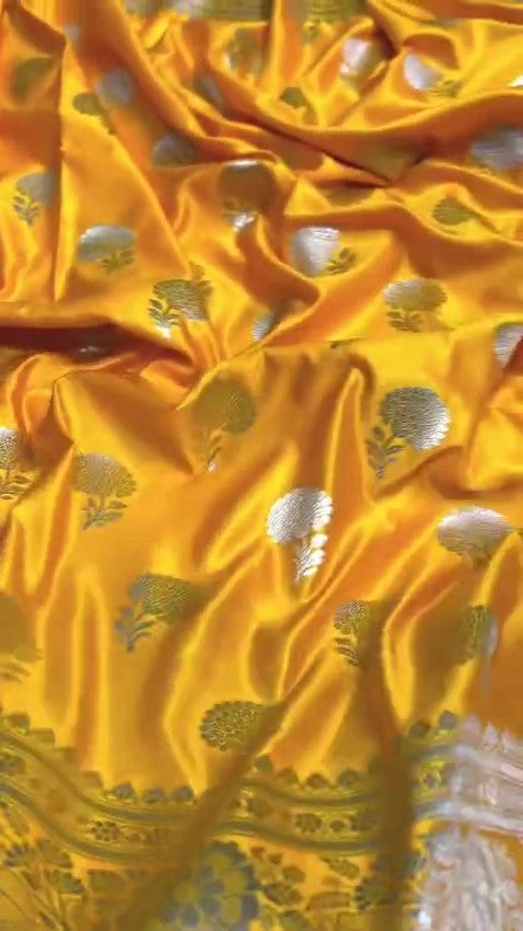 Radiant golden yellow Banarasi Mashru soft silk saree featuring intricate silver and gold zari work, a heavy floral border, and classic woven buttis.
