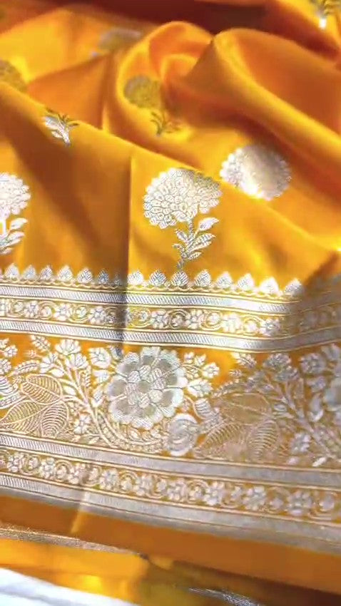 Radiant golden yellow Banarasi Mashru soft silk saree featuring intricate silver and gold zari work, a heavy floral border, and classic woven buttis.