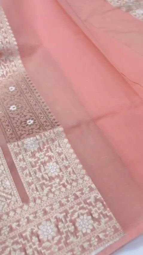Pastel peach Banarasi mercerised cotton saree with intricate Sona Rupa silver and gold zari weaving, posed against a modern architectural background.
