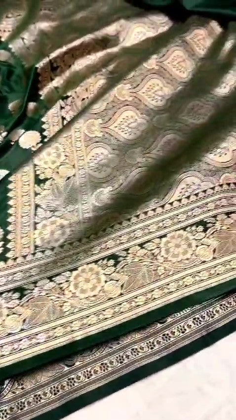A stunning deep bottle green Banarasi Mashru soft silk saree, adorned with intricate, traditional floral and paisley patterns handwoven using shining copper zari throughout the border, pallu, and body.