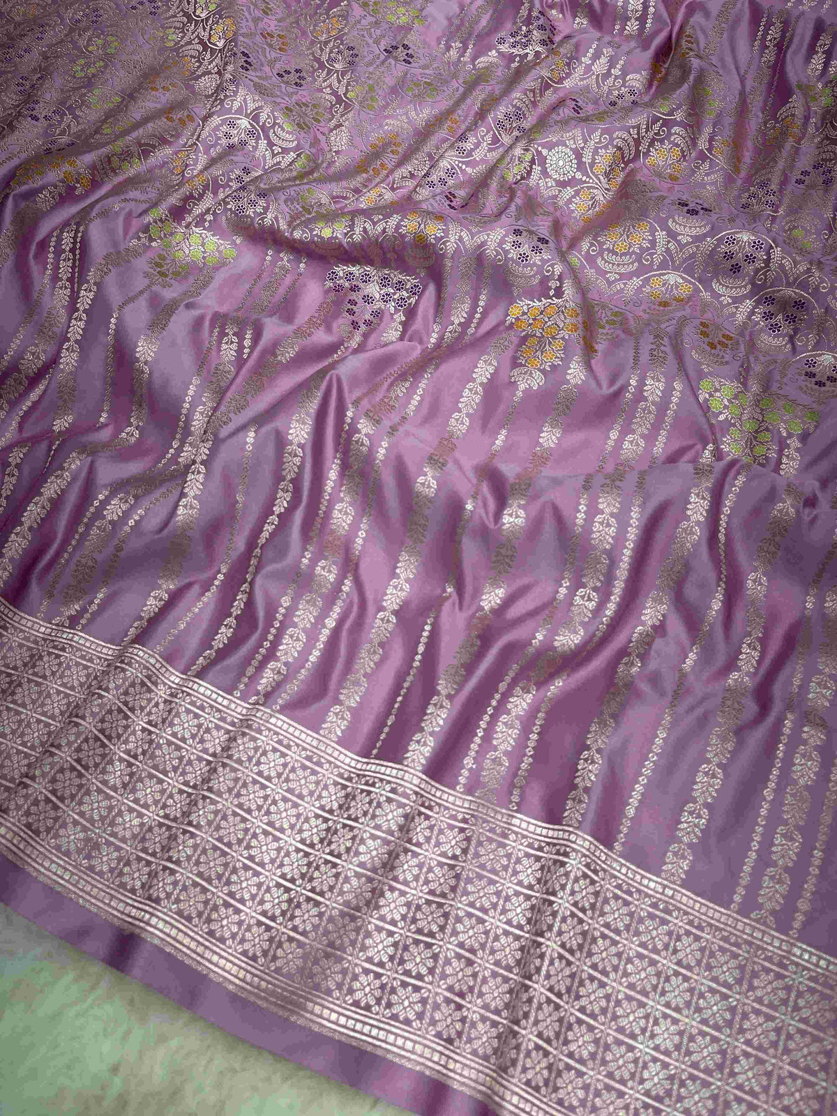 Folded lavender Banarasi mashru soft silk saree featuring intricate all-over floral jangla weave and subtle meenakari detailing.