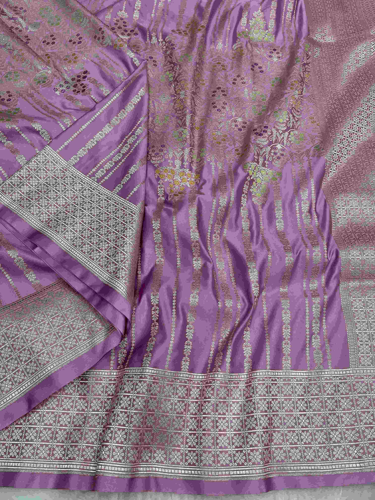 Folded lavender Banarasi mashru soft silk saree featuring intricate all-over floral jangla weave and subtle meenakari detailing.