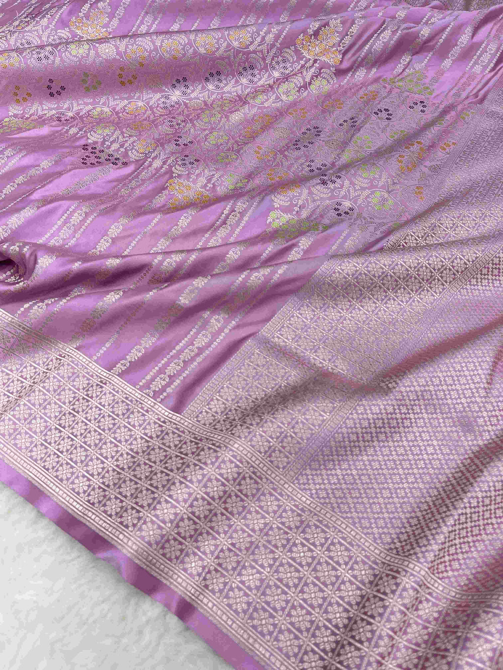 Folded lavender Banarasi mashru soft silk saree featuring intricate all-over floral jangla weave and subtle meenakari detailing.