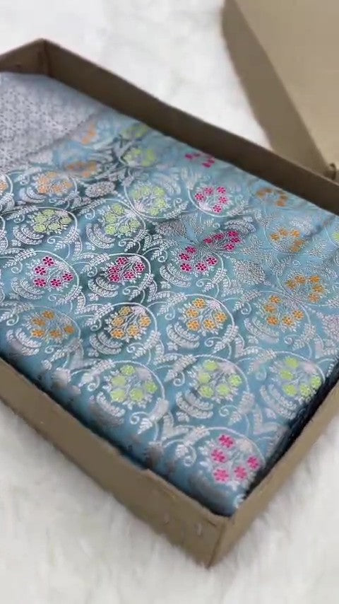 Light blue Banarasi mashru soft silk saree featuring all-over golden zari floral jangla weaving with pink, green, and yellow meenakari highlights and a silver geometric border.