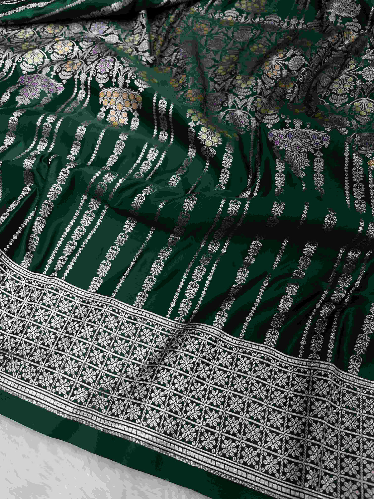 Bottle green Banarasi mashru soft silk saree featuring all-over golden zari floral jangla weaving, delicate meenakari highlights, and intricate zari borders.