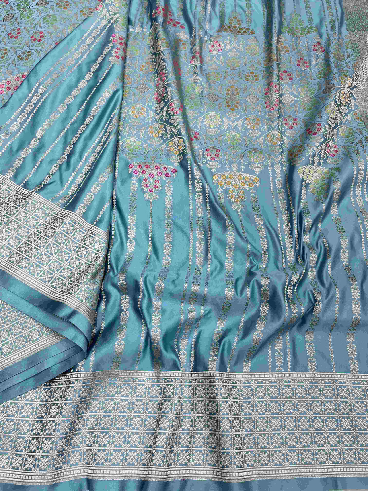 Light blue Banarasi mashru soft silk saree featuring all-over golden zari floral jangla weaving with pink, green, and yellow meenakari highlights and a silver geometric border.