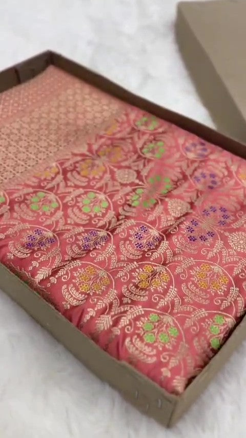 Folded coral pink Banarasi mashru soft silk saree woven with intricate all-over gold zari floral jangla and vibrant meenakari detailing inside a presentation box.