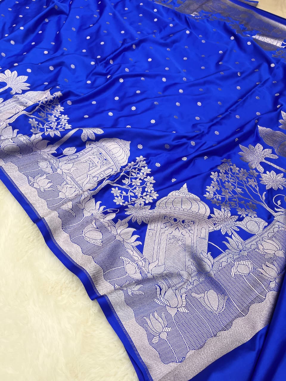 Royal Blue Banarasi Mashru soft silk saree featuring elaborate silver zari weaving of palace and floral motifs, captured in a luxurious, warm indoor setting.
