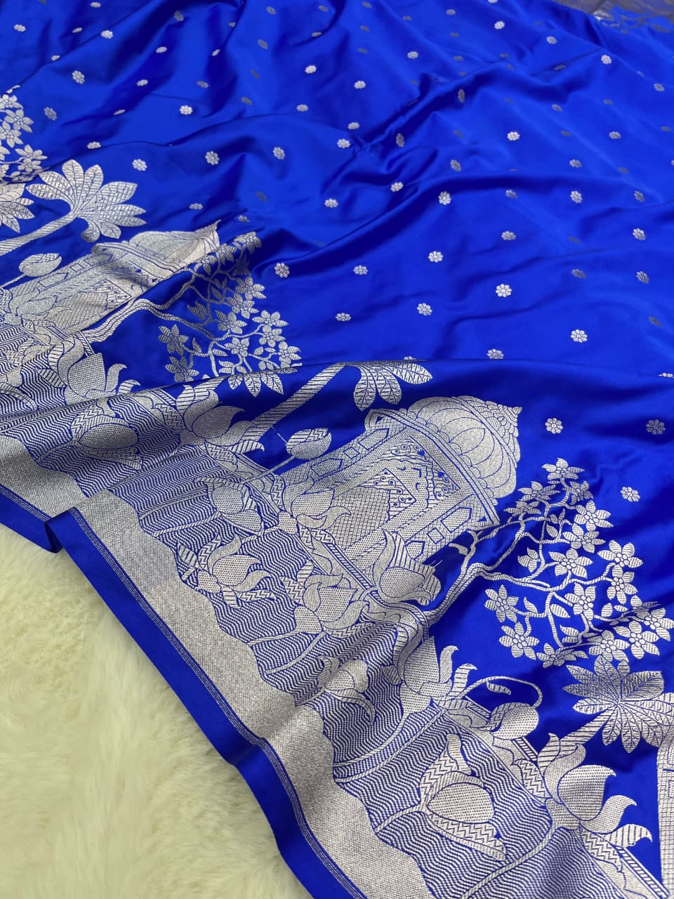 Royal Blue Banarasi Mashru soft silk saree featuring elaborate silver zari weaving of palace and floral motifs, captured in a luxurious, warm indoor setting.