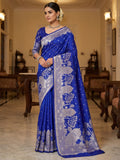 A model elegantly draped in a royal blue Banarasi Mashru soft silk saree featuring elaborate silver zari weaving of palace and floral motifs, captured in a luxurious, warm indoor setting.