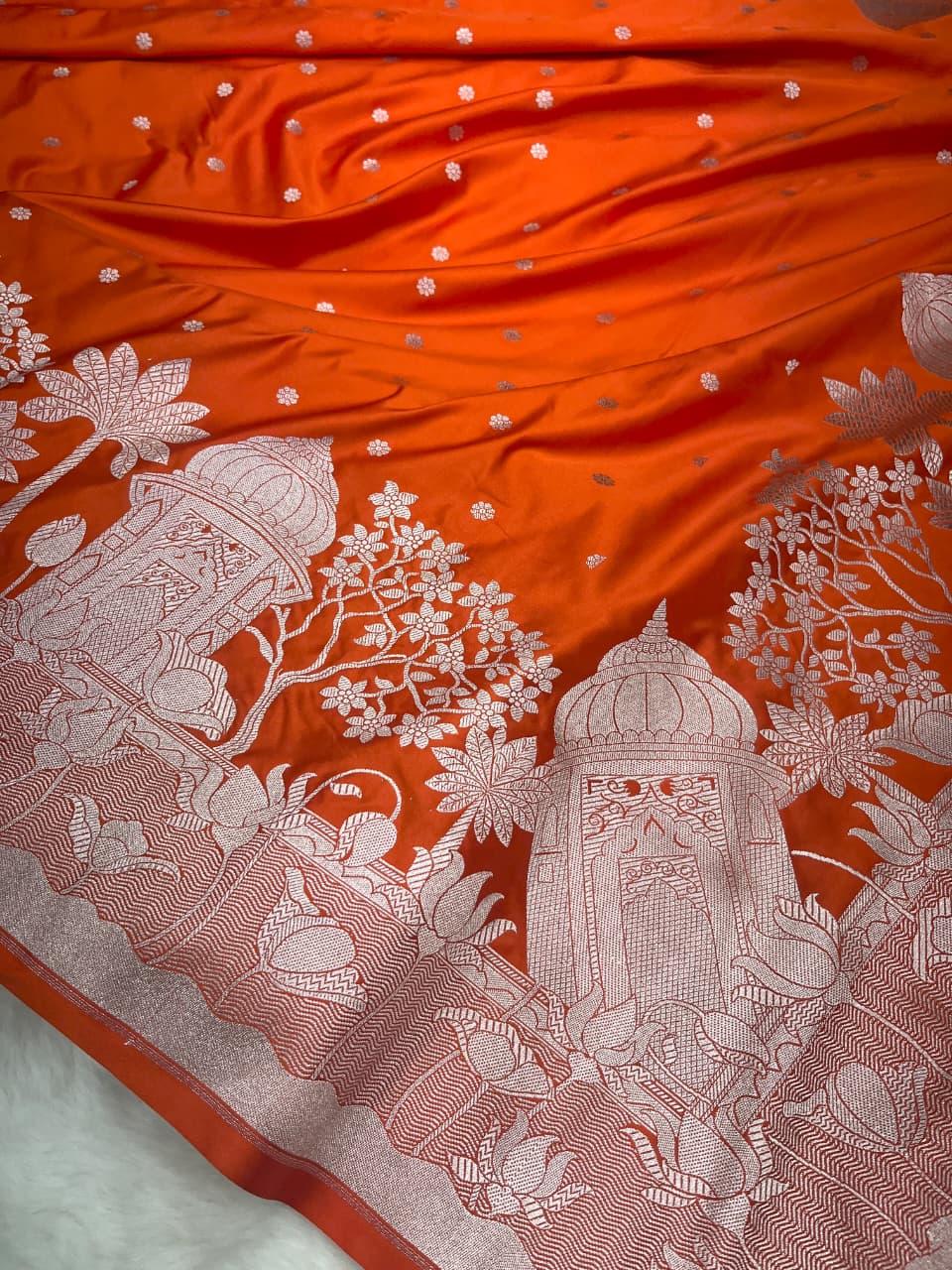 Vibrant orange Banarasi Mashru soft silk saree richly patterned with intricate silver zari work, including floral motifs and a detailed border.