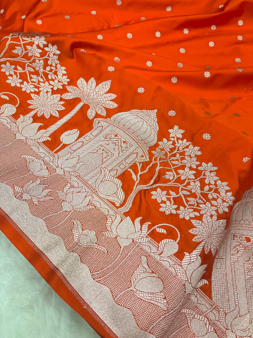 Vibrant orange Banarasi Mashru soft silk saree richly patterned with intricate silver zari work, including floral motifs and a detailed border.