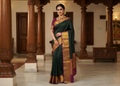 A woman wearing a luxurious bottle green Kanchipuram handloom 2G silk saree with 8-color temple border, traditional gold zari, and vibrant purple accents, perfect for weddings and festive occasions.