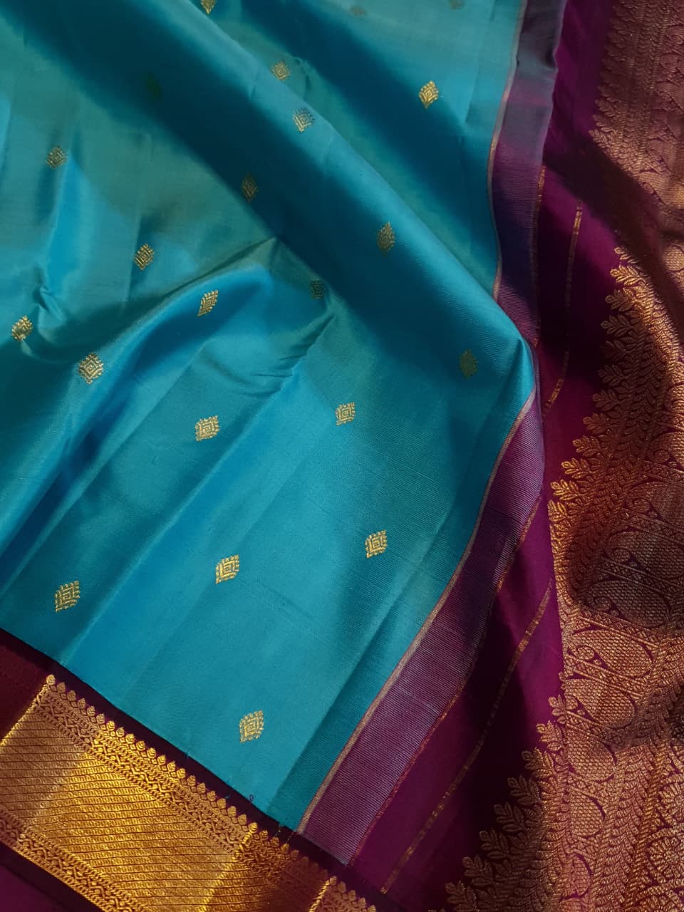 Vibrant turquoise blue Kanchipuram handloom silk saree with a contrasting deep purple korvai border and intricate gold zari work.