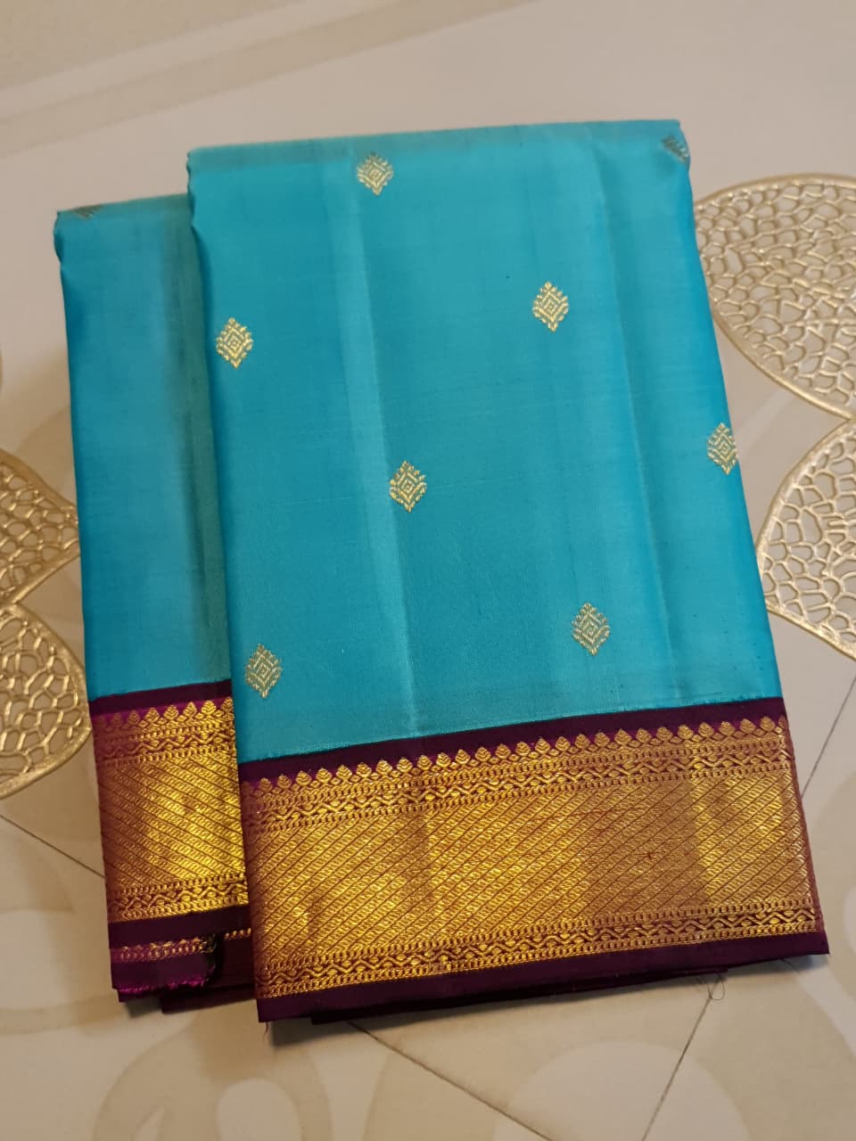 Vibrant turquoise blue Kanchipuram handloom silk saree with a contrasting deep purple korvai border and intricate gold zari work.