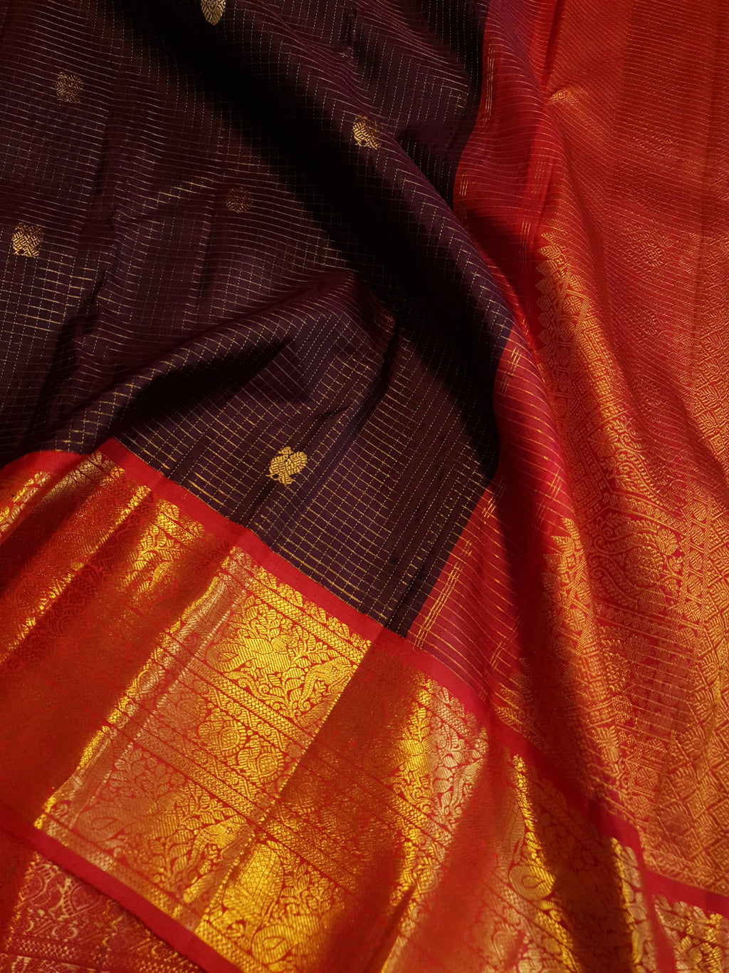 Dark plum Kanchipuram silk saree featuring a gold Muthukattam check pattern, ornate zari buttas, and a vibrant contrast border and pallu.